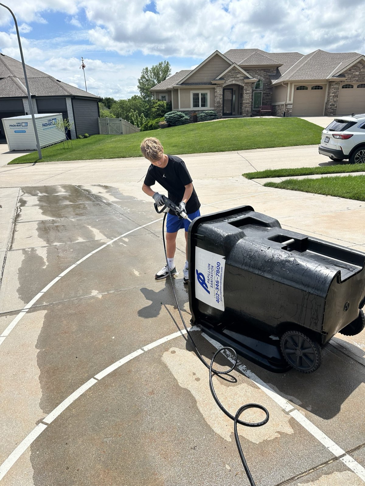 Premier Bin Cleaning pressure-washing a curbside trash bin in a driveway